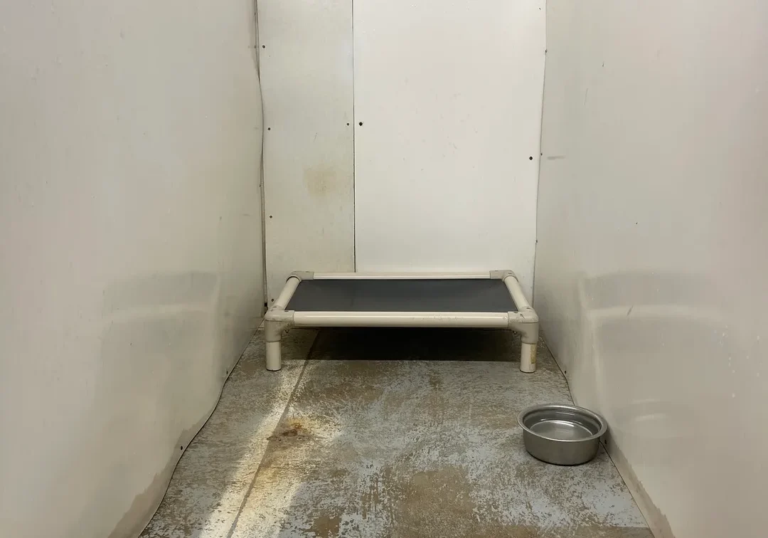 A small room with a metal bed and concrete floor.